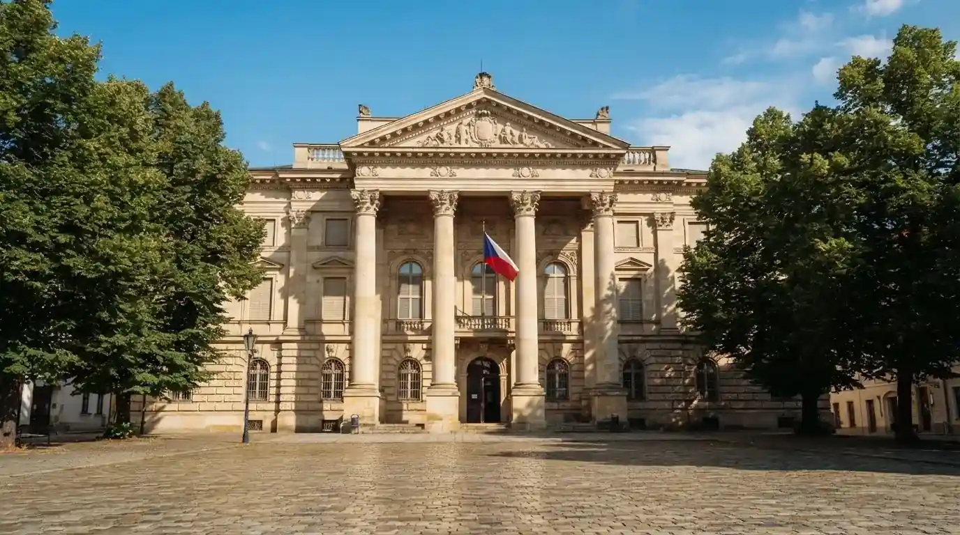 Kamenná budova se sloupy a vlajkou stojí na náměstí za slunečného dne.